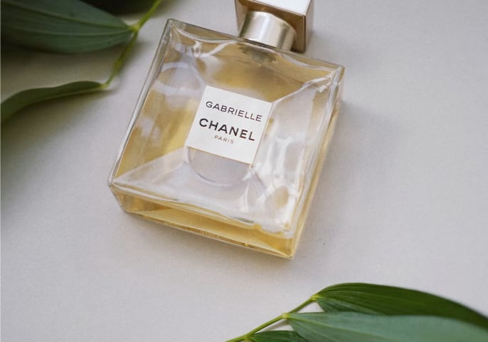 Chanel perfume bottle on a table with green leaves on either side